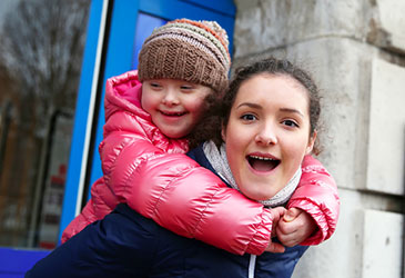 A woman and a child smile joyfully together outdoors in a sunny setting.