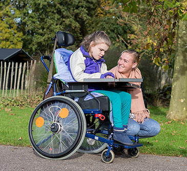 A woman in a wheelchair, smiling and looking confidently at the camera in an outdoor setting.